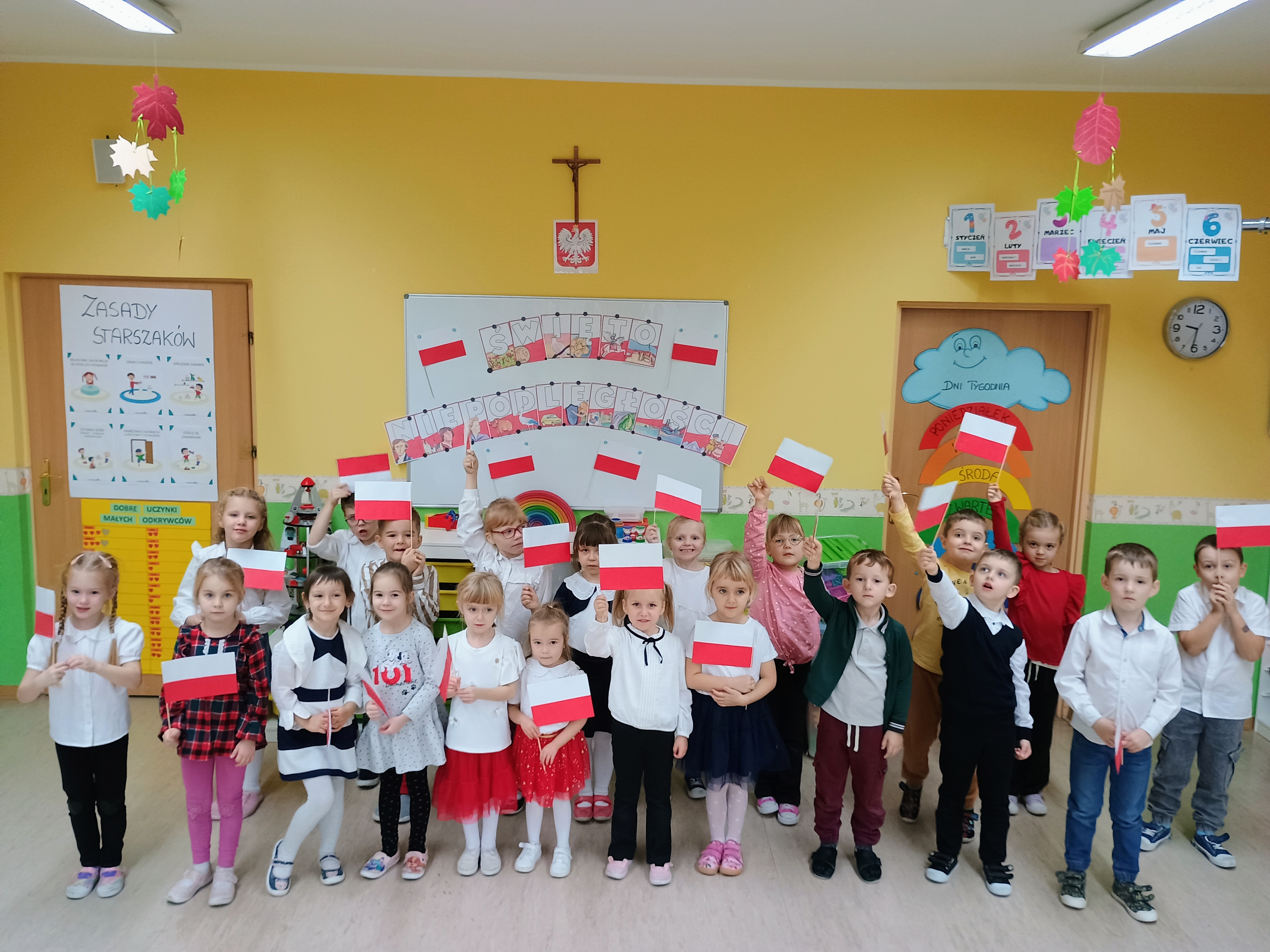 Grupa starszaków  pozuje na tle napisu dzień niepodległości z flagami