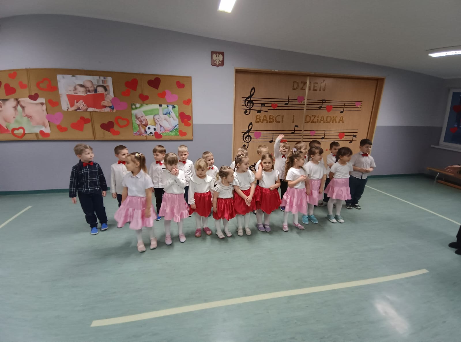 Młodsze dzieci śpiewają i mają ubrane kolorowe spódniczki.